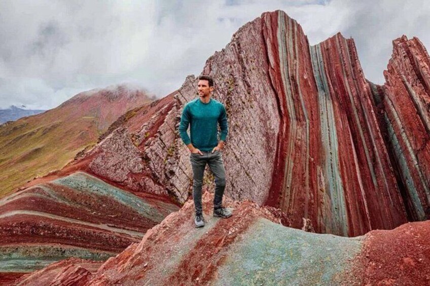 A person standing on a colorful rock formation with a mountain in the background. 5