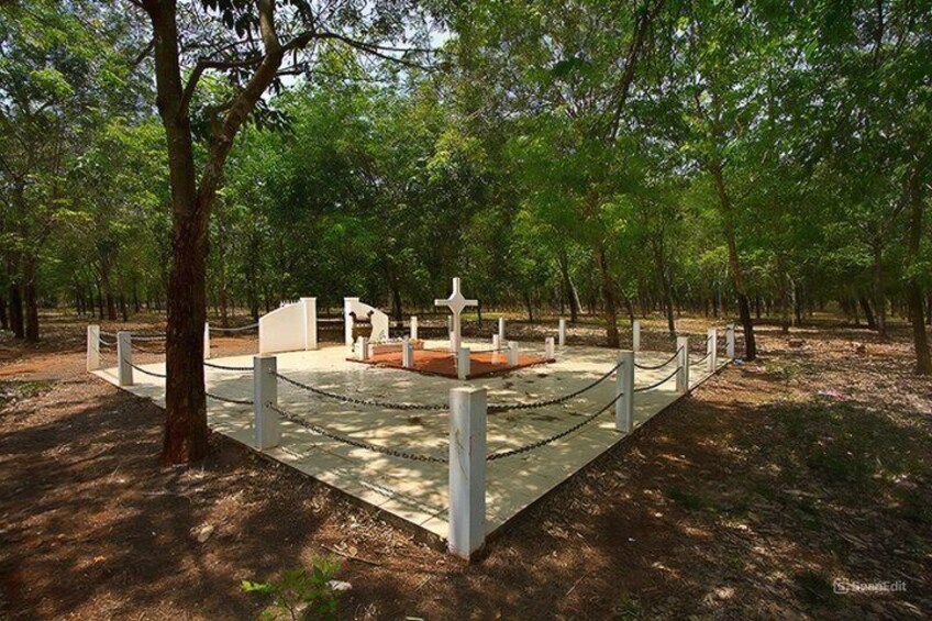 A fenced memorial area with crosses and a central monument surrounded by trees. 3