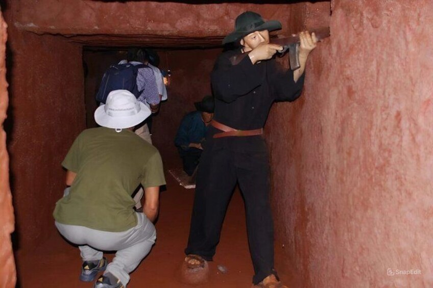 People in a narrow passageway, one person crouching and another holding a flashlight. 2