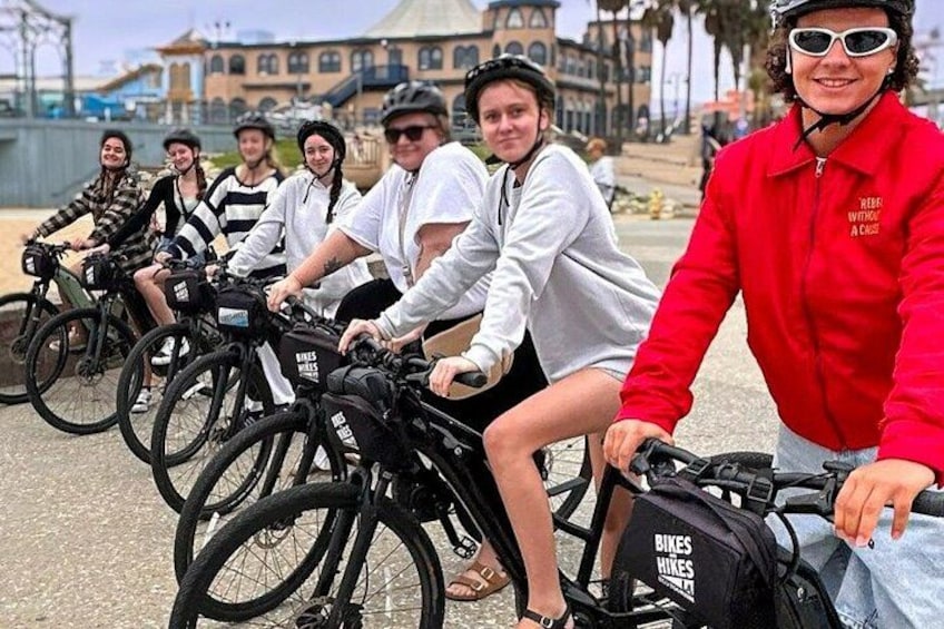 A group of people on bicycles, some wearing casual clothing, in an urban setting with buildings and a waterfront in the background. 3