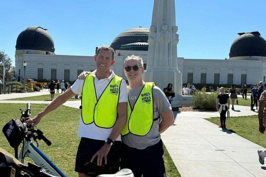 Two people wearing safety vests with a building and domed structures in the background. 5