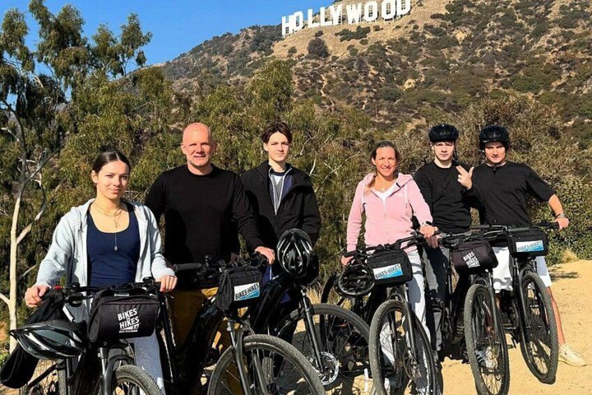 A group of people with bicycles in front of a hill with the Hollywood sign. 2