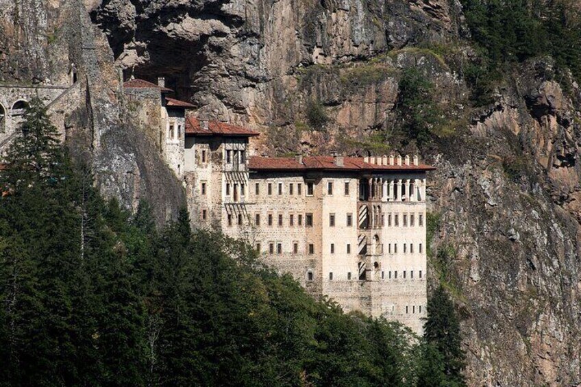 A historic building nestled in a rocky cliffside, surrounded by dense forest. 5