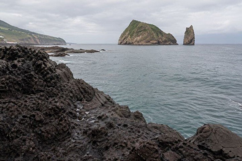 A rocky coastline with a prominent rock formation and a smaller island in the distance. 2