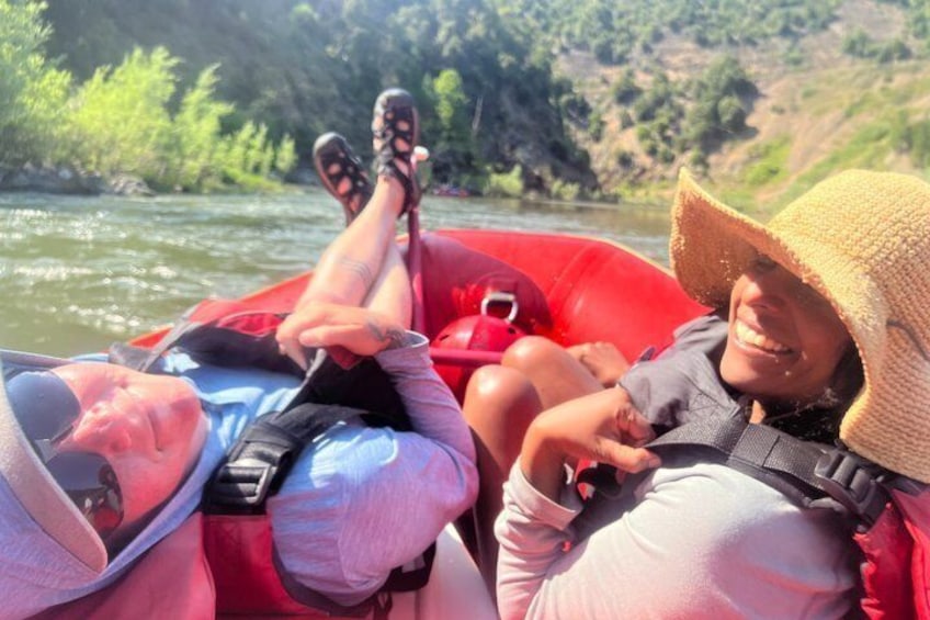 Two people in a red inflatable raft on a river surrounded by greenery. 1