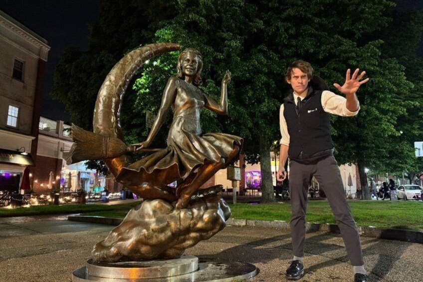 A bronze statue of a woman with a crescent moon, a man in a vest and tie, and a cityscape in the background. 1