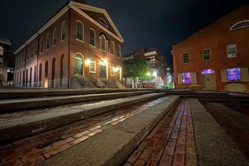 A brick building with arched windows and a staircase leading up to the entrance, illuminated by street lamps. 3