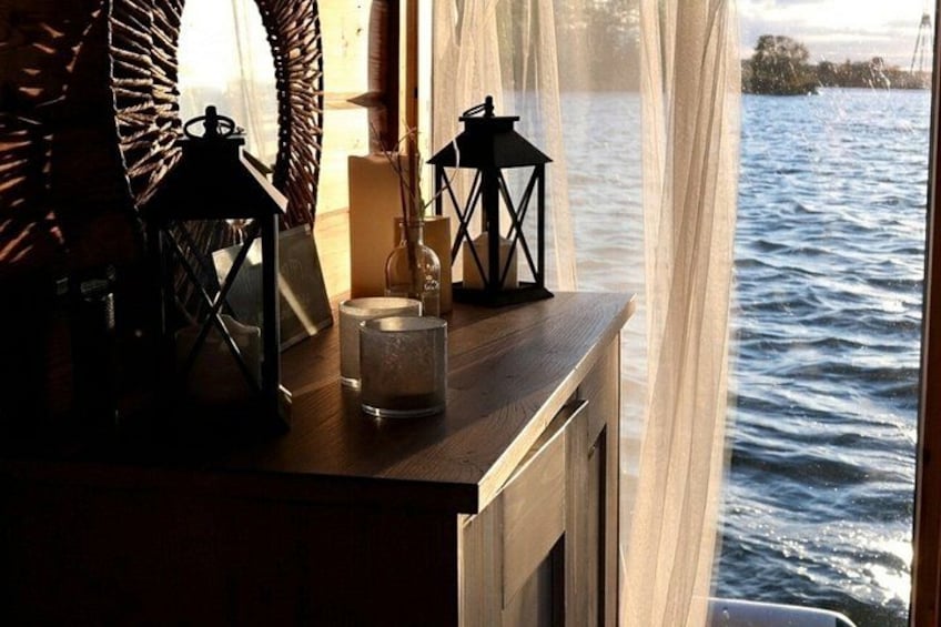 A wooden table with lanterns and candles by a window overlooking a body of water. 4