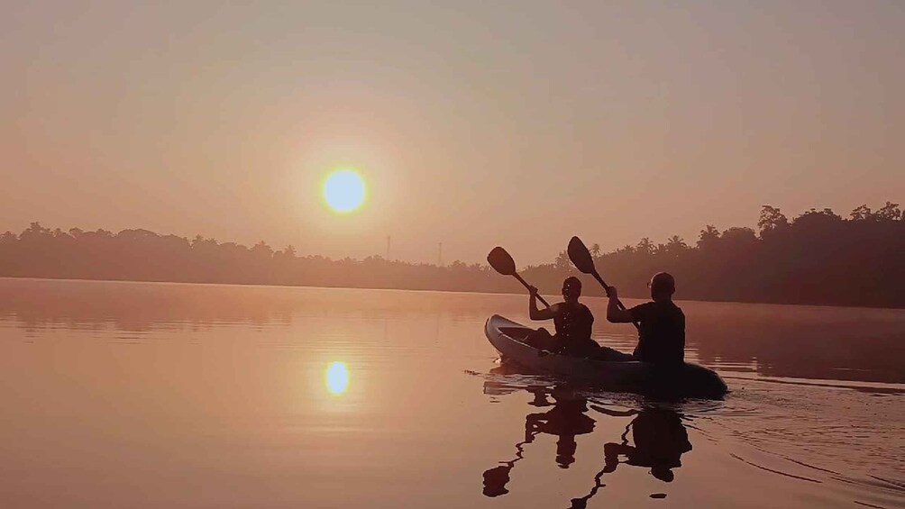 A sunrise over a calm lake with two people kayaking. 5