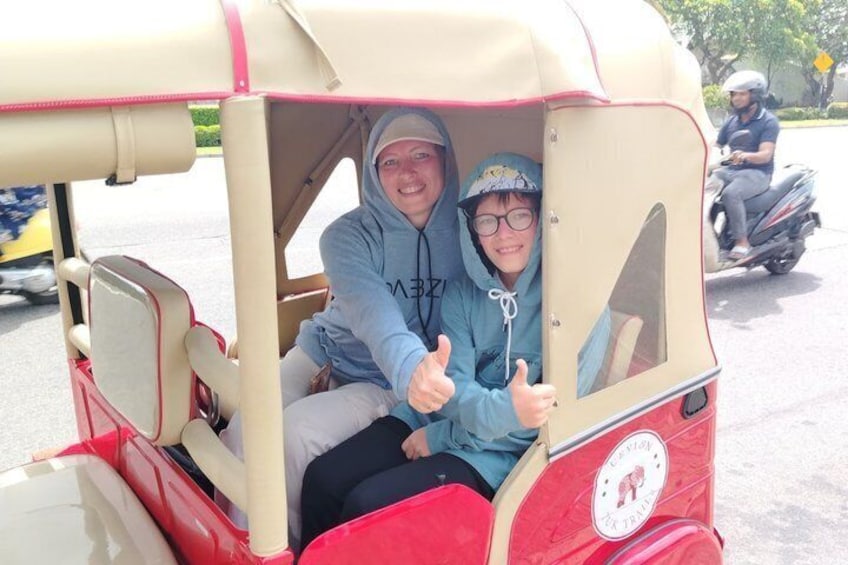 A vintage car with two people inside, one giving a thumbs up. 3