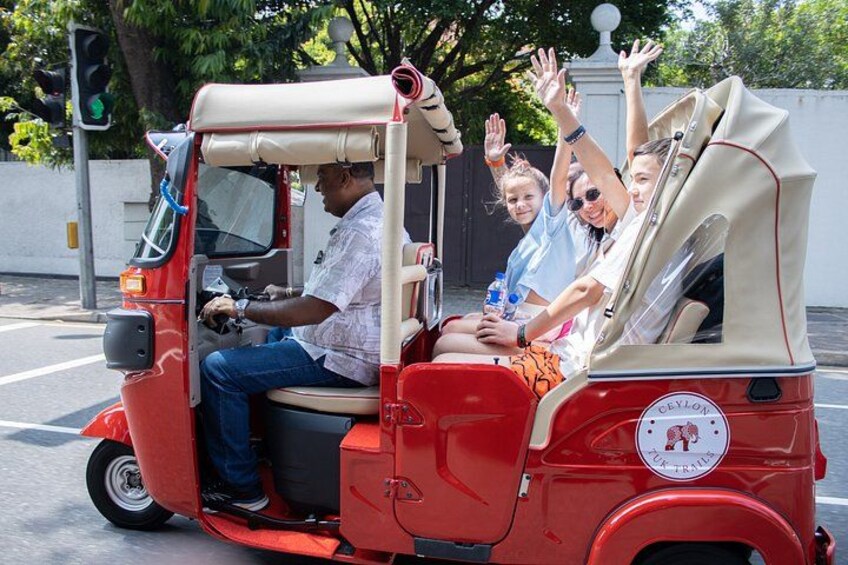 En rød tuk-tuk med passagerer, der vinker. 1