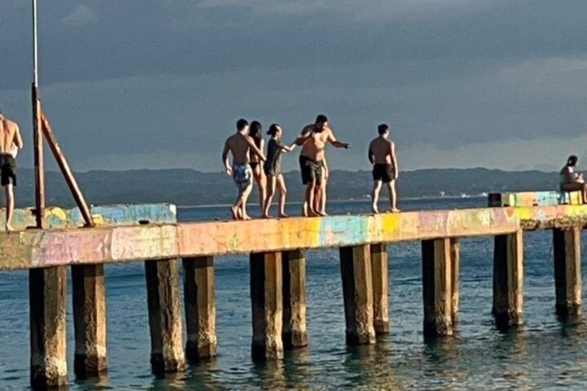 A pier with people standing at the end, a body of water, and distant mountains. 5
