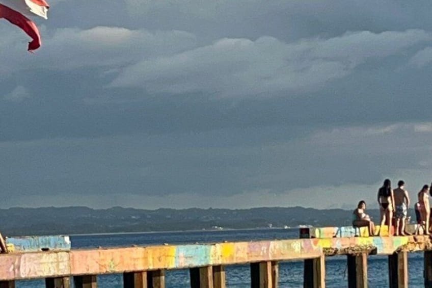 A pier with people standing at the edge, overlooking a body of water and distant mountains. 4