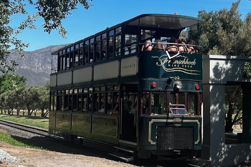 A vintage tram with passengers, traveling on tracks, surrounded by trees and mountains. 5