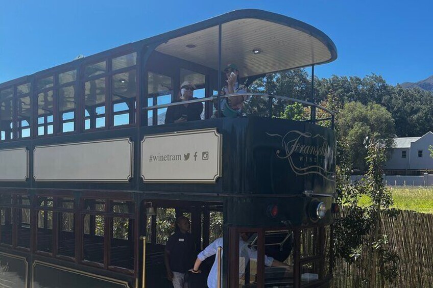 A vintage tram with 'Franz's Wine' branding, passengers, and a rural landscape with houses and trees. 4