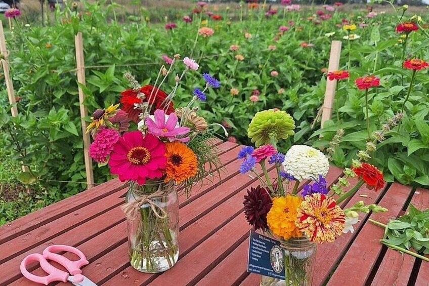 Two glass vases with colorful flowers on a wooden table, surrounded by a garden with various plants. 3