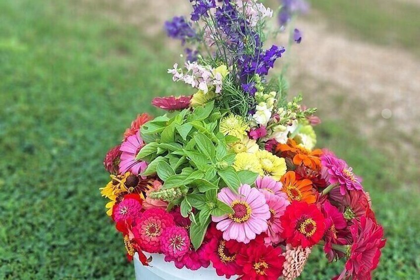 A bouquet of flowers in a white vase on a grassy surface. 2