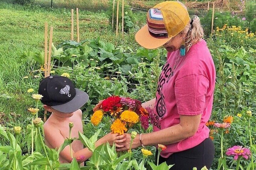 A person holding a bouquet of flowers in a garden with various plants and a child in the foreground. 1