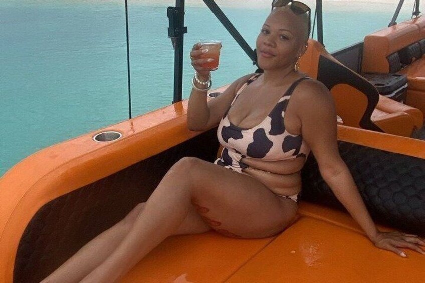 A person in a patterned swimsuit on a boat with a drink, surrounded by water. 2