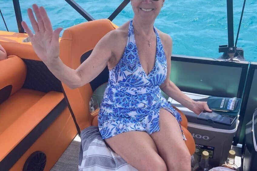 A person seated on a boat with a blue and white patterned dress, holding a device, and waving. 5