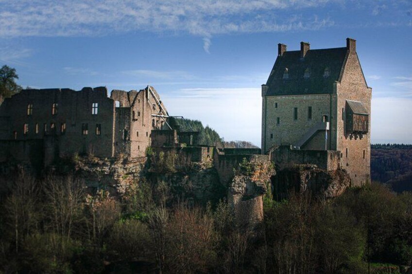 A historic castle with ruins and a tower, surrounded by trees and a clear sky. 1