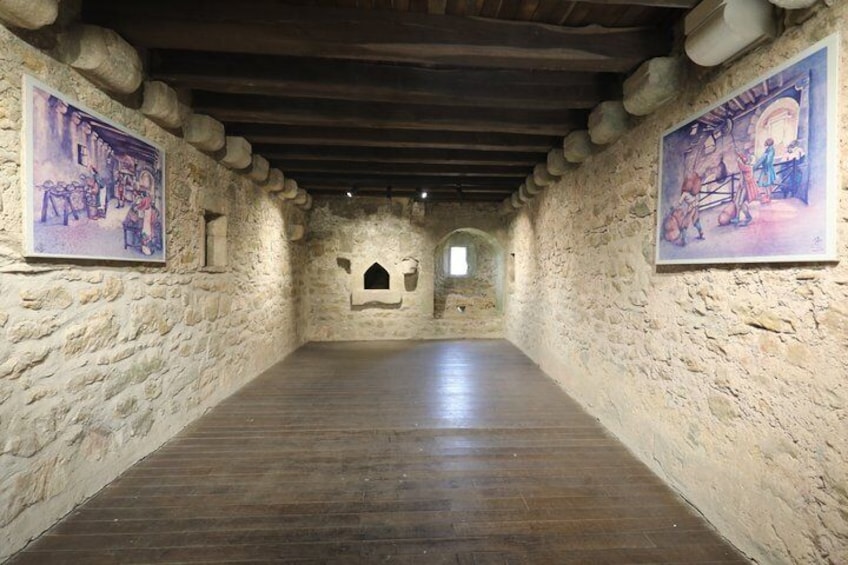 A stone-walled corridor with wooden flooring and two paintings on the walls. 3
