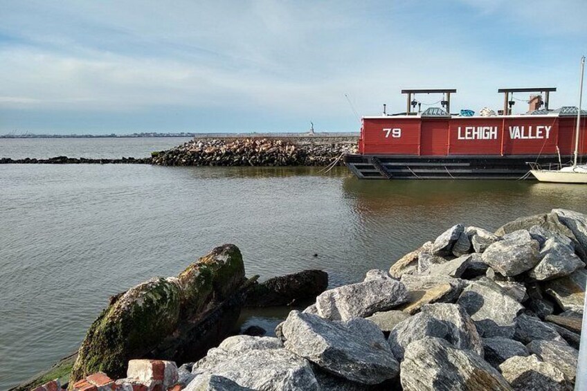A red boat named 'Lehigh Valley' with the number 79, docked at a rocky pier with calm water in the background. 1