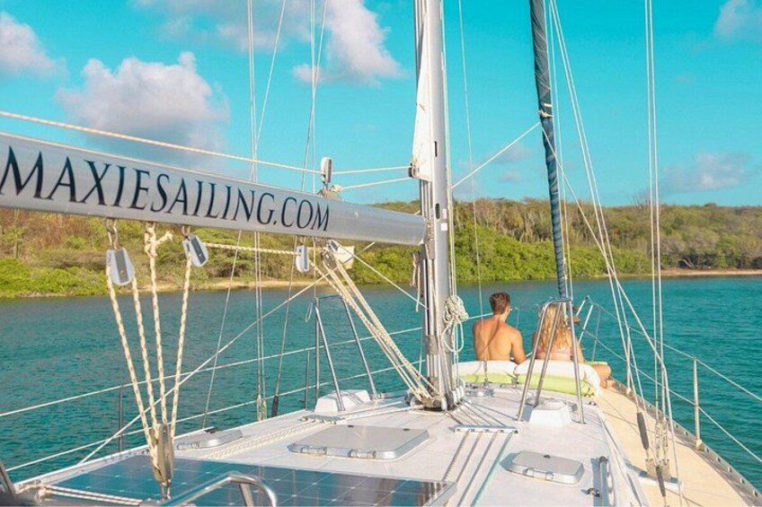 A sailboat with two people on deck, calm water, and a clear sky. 5