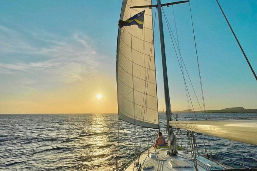 A sailboat with a flag, calm sea, and a sunset. 2