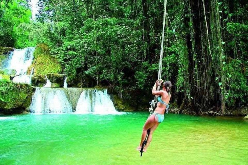 A person swinging on a rope over a waterfall in a forested area. 1