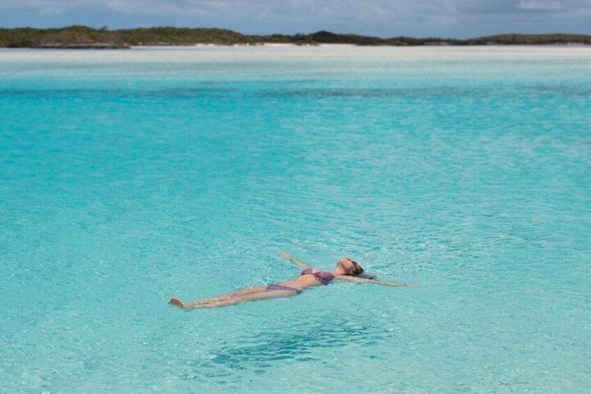 A person floating on a clear turquoise sea with a distant shoreline. 4
