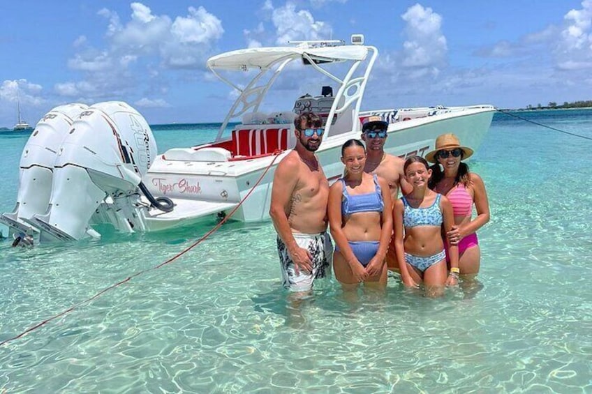 A group of people standing in shallow water next to a boat named 'Tiger Shark.' 1