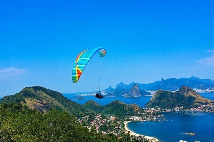 A paraglider over a coastal landscape with mountains and a clear sky. 1