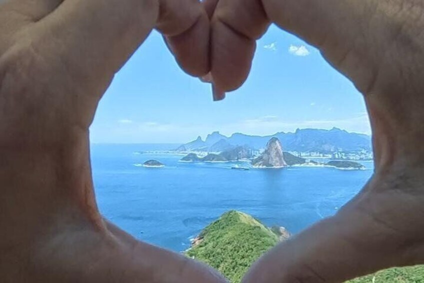 Hands framing a view of a coastal landscape with mountains and a prominent rock formation. 5