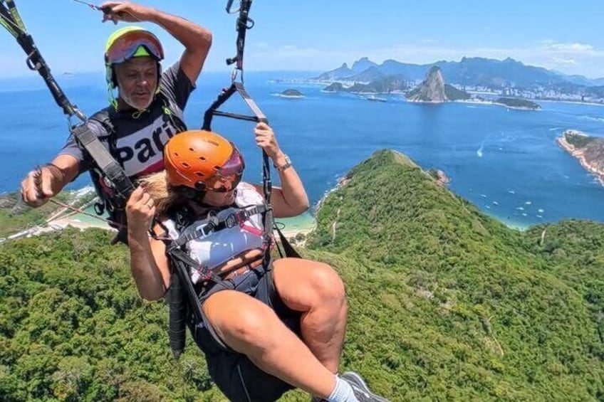 Two people on a tandem paragliding adventure with a coastal landscape in the background. 2