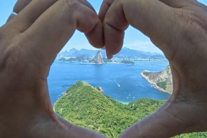 Hands forming a heart shape framing a coastal landscape with mountains and greenery. 3