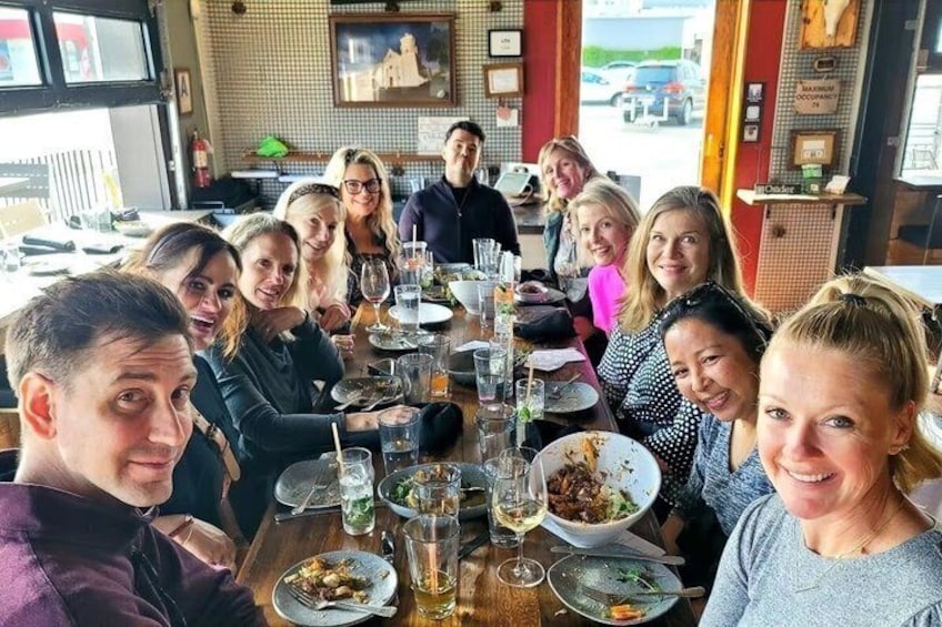 A group of people seated around a table in a restaurant with various dishes and drinks. 3