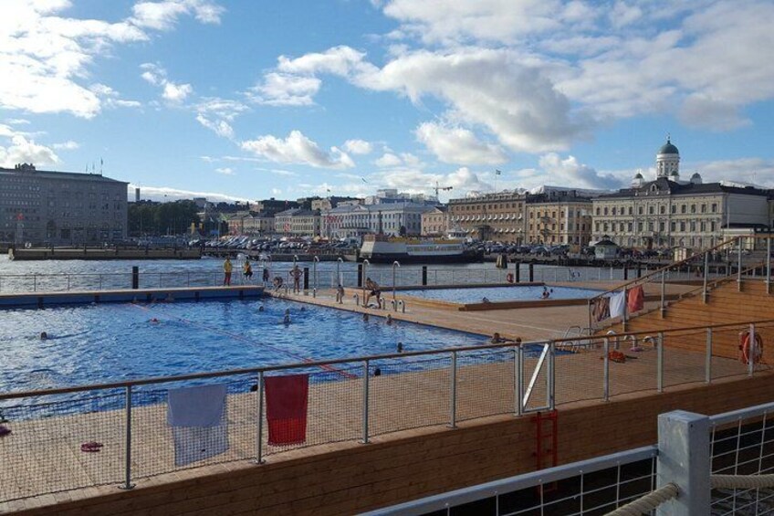 A swimming pool with a wooden deck, a lifebuoy, and a distant cityscape with buildings. 4