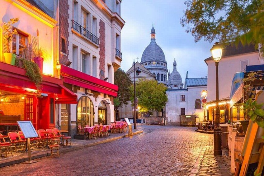 A cobblestone street lined with red awnings and outdoor seating, leading to a domed building. 4