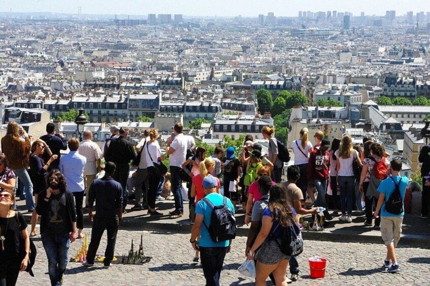 A crowded viewpoint overlooking a cityscape with buildings and a distant skyline. 3