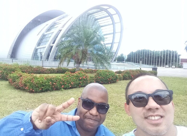 Two people taking a selfie with a modern building and landscaped garden in the background. 4