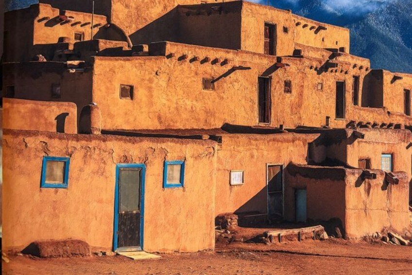 A traditional adobe building with blue window frames and a door. 4