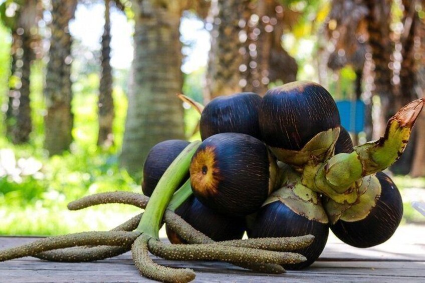 A bunch of dark purple, round fruits with green stems and leaves, lying on a wooden surface outdoors. 3