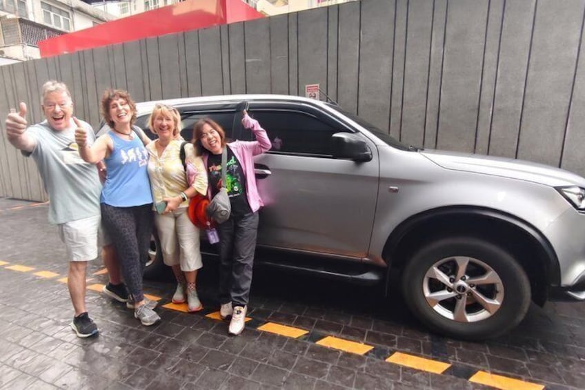 Four people standing in front of a silver SUV on a wet pavement. 2
