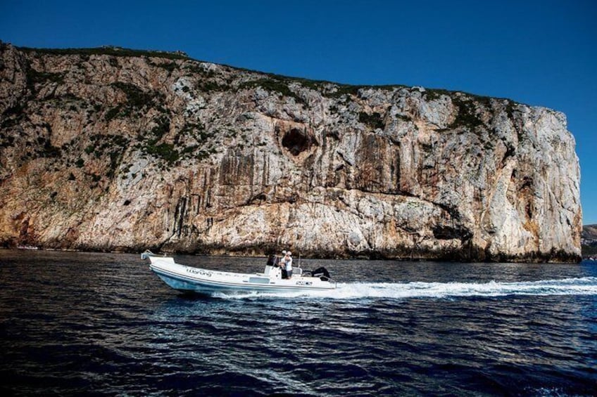 A boat on a body of water with a rocky cliff in the background. 3