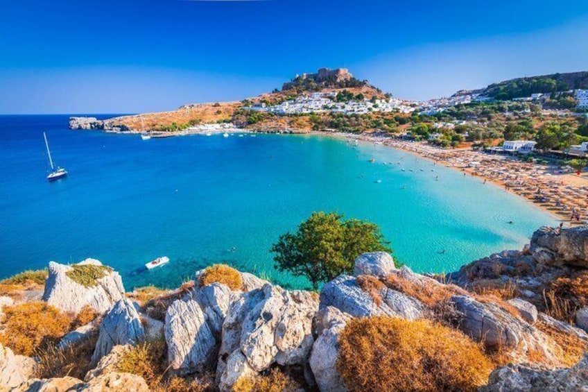 A coastal landscape with clear turquoise waters, rocky outcrops, and a small settlement on a hill. 3