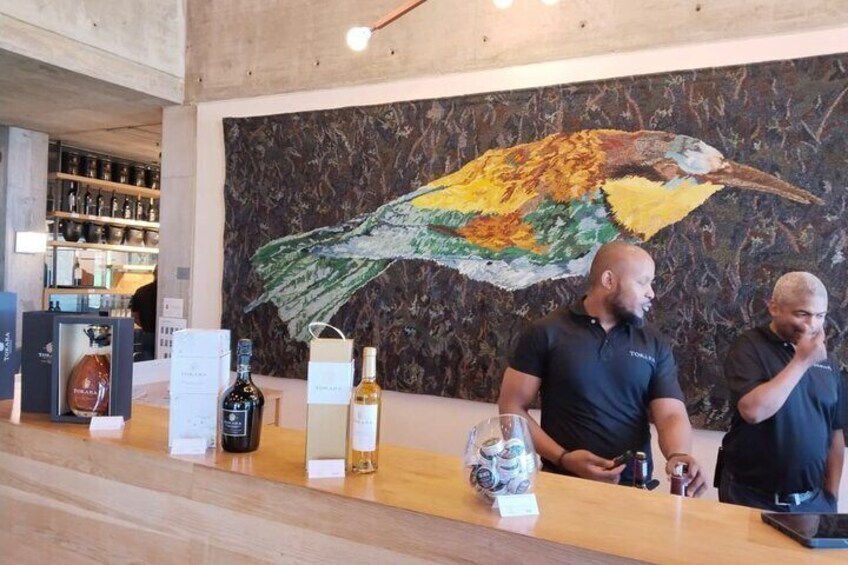 A bar with a large bird mural, bottles of alcohol, and two people standing behind the counter. 2