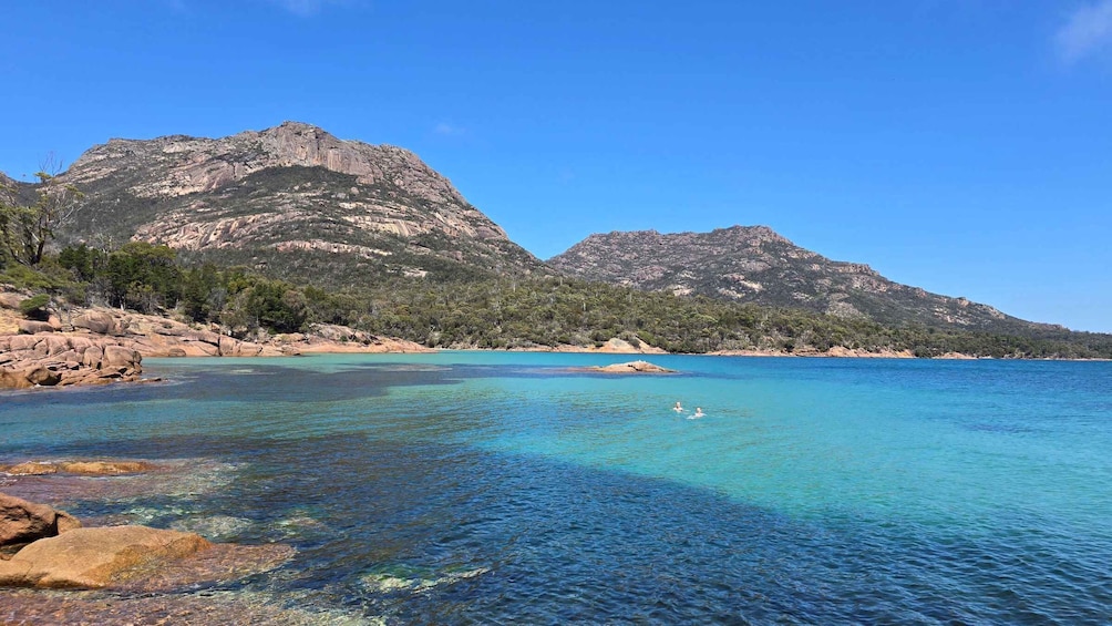 A coastal landscape with clear turquoise waters, rocky shores, and forested hills. 4