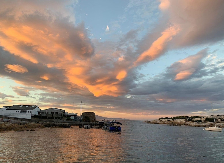 A waterfront with boats, a white building, and a rocky outcrop under a sunset sky. 2