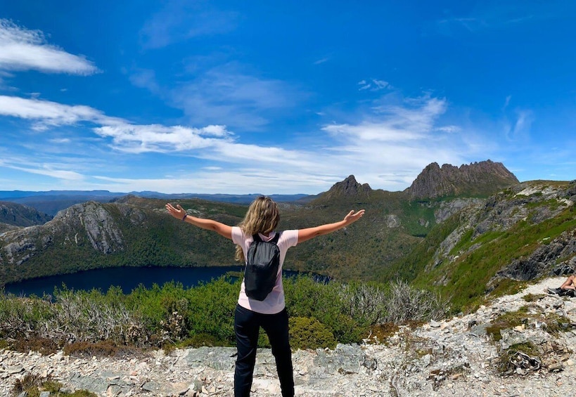 A person standing on a rocky outcrop with arms outstretched, overlooking a mountainous landscape and a lake. 1